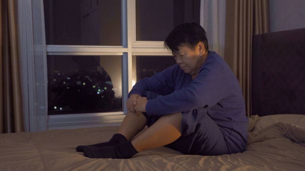 Przygnębiony samotny starsza Azjatka, ludzie siedzący na łóżku z oknami i widok na miasto w sypialni w domu. Styl życia późną nocą. Bezsenność. Kwarantanna - Zdjęcie, obraz