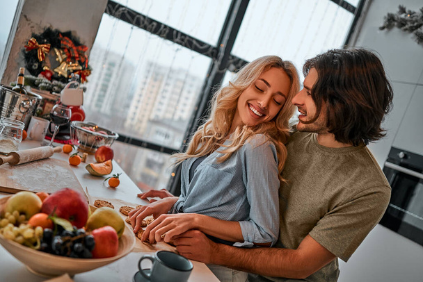 Happy young couple preparing cookies together in the kitchen at home. Christmas time - Фото, изображение