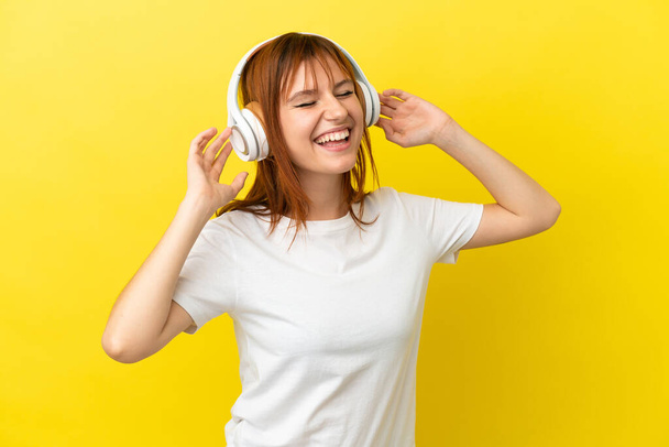 Redhead girl isolated on yellow background listening music and singing - Foto, Imagem