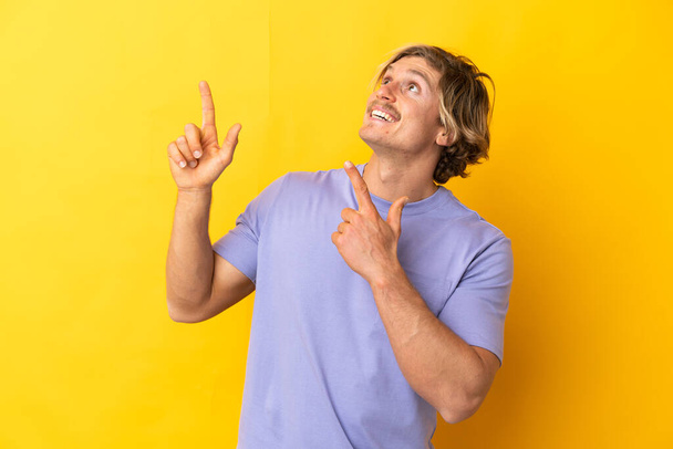 Hombre guapo rubio aislado sobre fondo amarillo apuntando con el dedo índice una gran idea - Foto, Imagen