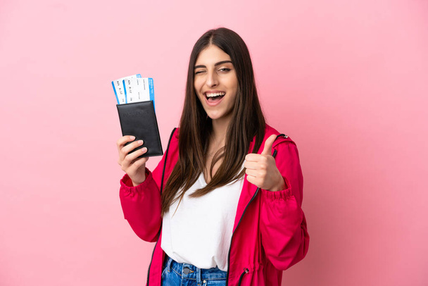 Young caucasian woman isolated on pink background in vacation holding a passport and plane with thumb up - Фото, изображение