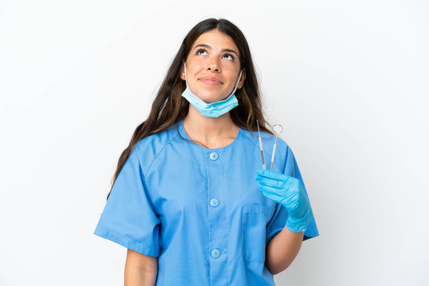 Mujer dentista sosteniendo herramientas sobre fondo blanco aislado y mirando hacia arriba - Foto, Imagen