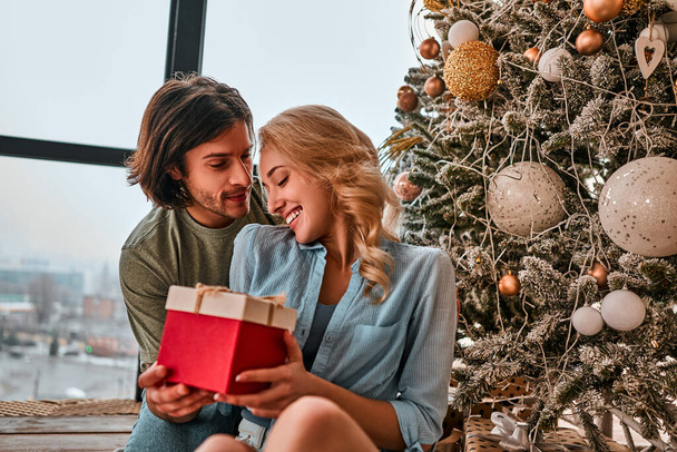 Cute, young couple exchanging Christmas presents on Christmas morning. Close up view - Фото, изображение
