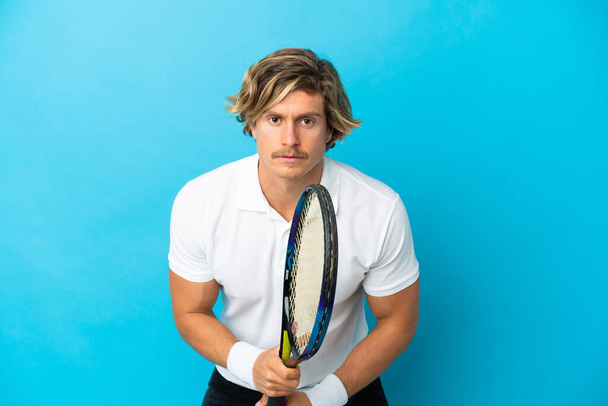 młody blondynka człowiek odizolowany na niebieskim tle gra w tenisa - Zdjęcie, obraz