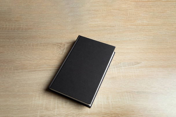 Black book on wooden background. - Zdjęcie, obraz