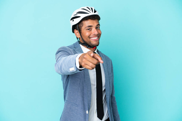 Jeune homme d'affaires brésilien avec casque de vélo isolé sur fond bleu pointe du doigt vers vous avec une expression confiante - Photo, image