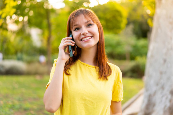 Jovem mulher ruiva bonita ao ar livre mantendo uma conversa com o telefone celular com alguém - Foto, Imagem