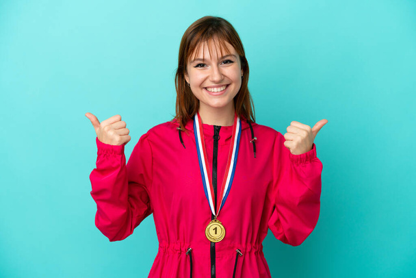 Zrzka dívka s medailemi izolované o modré pozadí s palci nahoru gesto a úsměv - Fotografie, Obrázek
