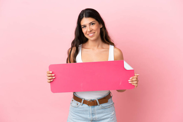 Junge kaukasische Frau isoliert auf rosa Hintergrund mit einem leeren Plakat - Foto, Bild