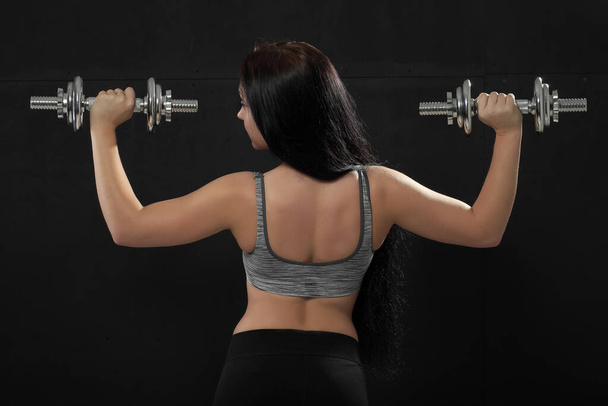 Atletik genç bir kadın koyu arka planda ağırlık çalışıyor. - Fotoğraf, Görsel