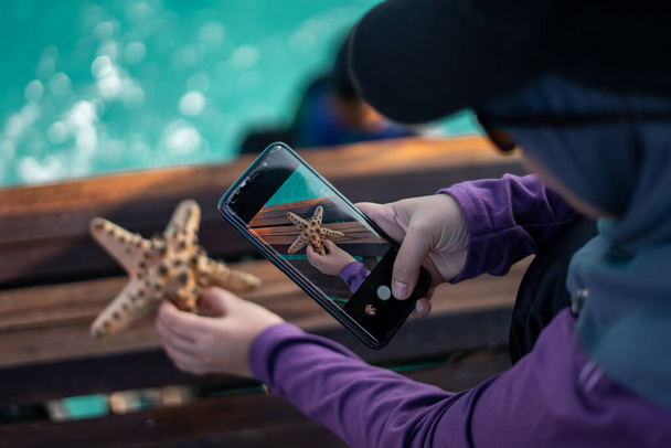 Женщина фотографирует морскую звезду на тропической морской палубе. - Фото, изображение