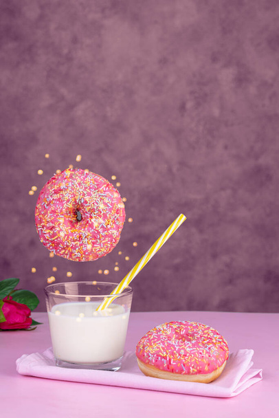 Flying pink donut with a glass of milk on a pink background - Foto, Bild