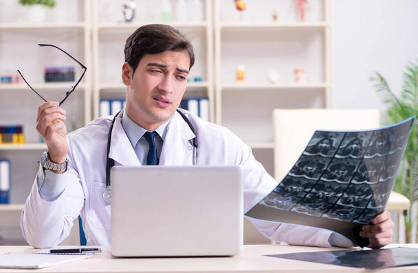 Médico joven mirando imágenes de rayos X en la clínica - Foto, Imagen