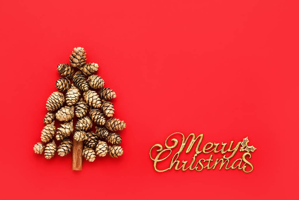 Merry Christmas card. Christmas tree made from golden cones and text Merry Christmas on a red background. Copy space - Photo, Image