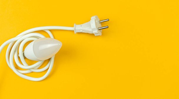 Saving energy with LED light bulb and electrical power cable, yellow background, banner, top view and flat lay with copy space photo - Photo, image