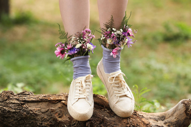 Woman standing on log with flowers in socks outdoors, closeup - Foto, Bild
