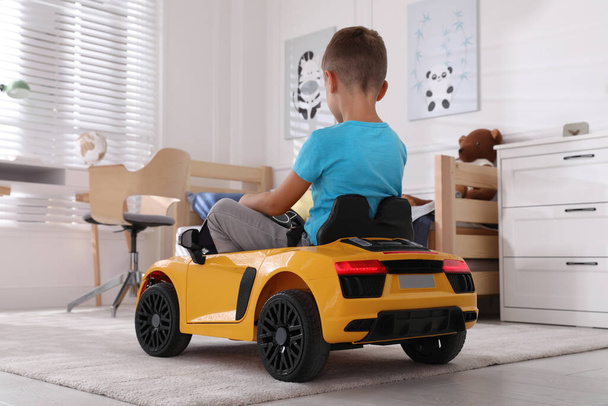 Cute little boy driving big toy car at home, back view - Foto, afbeelding