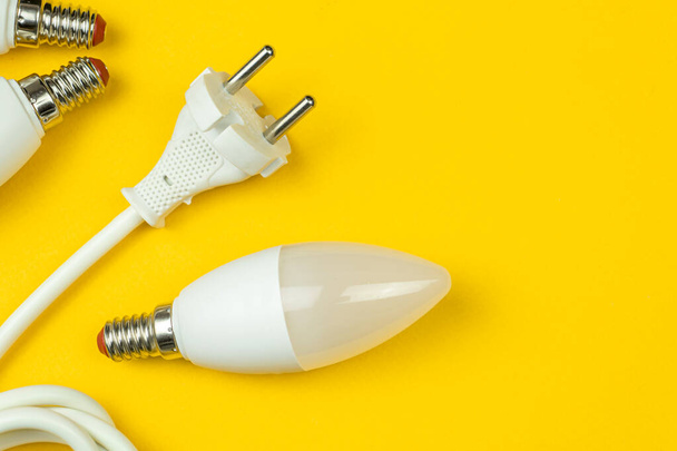 Eficiencia energética verde con bombillas led y cable de alimentación eléctrica con enchufe UE. Fondo amarillo, plano y vista superior - Foto, imagen