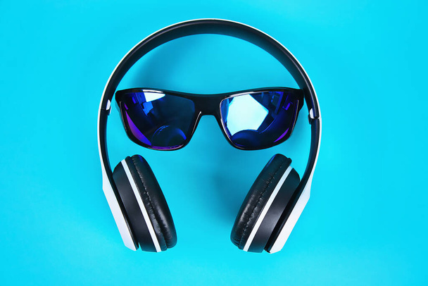 Sunglasses in white wireless headphones on blue background. The concept of rest, relaxation. - Foto, imagen