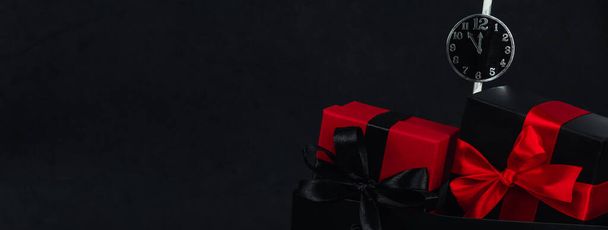 One package with two gift boxes and a paper clock on the right against a black background with space for text on the left, close-up side view. Christmas and black friday concept. - Photo, Image