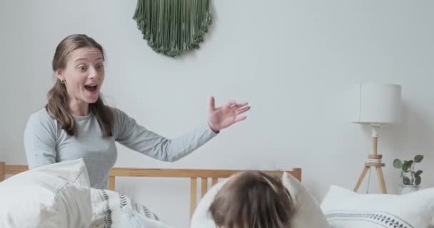 Nahaufnahme glücklicher Junge, der auf dem Bett springt, umgeben von bequemen Baumwollkissen, die mit Kindermädchen spielen - Filmmaterial, Video