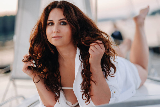 sexy woman in a white shirt enjoys the sunset on her private white yacht. - Zdjęcie, obraz