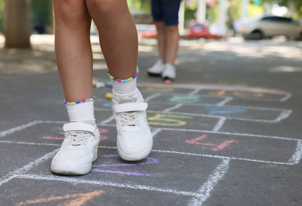Little children playing hopscotch drawn with chalk on asphalt outdoors, closeup - Photo, Image