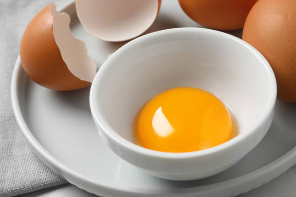 Chicken eggs and bowl with raw yolk on table, closeup - Photo, Image