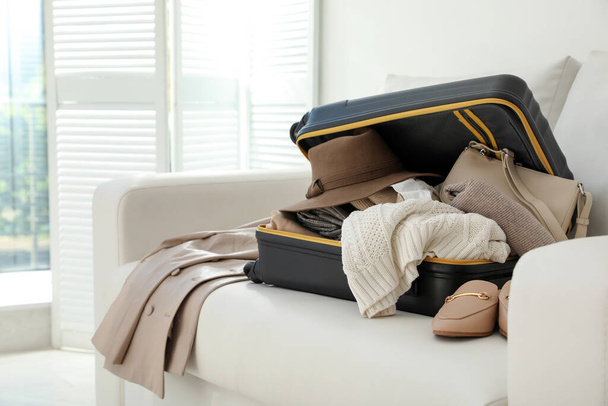 Open suitcase full of clothes, jacket and fashionable shoes on sofa in room - Foto, Bild