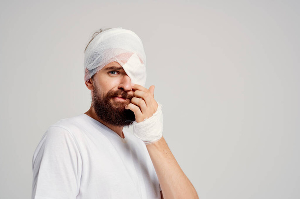 männlicher Patient mit bandagiertem Kopf und Augen-Krankenhausaufenthalt Licht Hintergrund - Foto, Bild