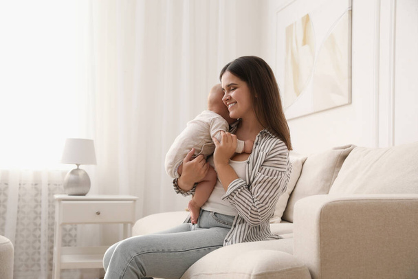 Young woman with her little baby on sofa at home - Foto, Bild