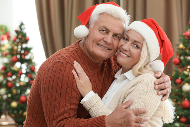 Happy mature couple in Santa hats at home. Christmas celebration - Fotografie, Obrázek