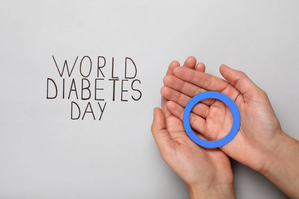 Woman holding blue paper circle near text World Diabetes Day on light background, top view - Foto, Bild