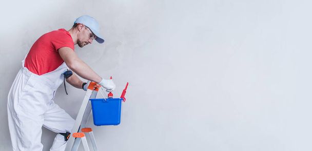 Trabalhador contratante de pintor de interiores em uma escada preparando-se para um trabalho de pintura de apartamento. Espaço de cópia lateral direita. - Foto, Imagem