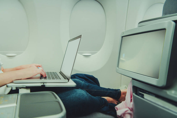 Mujer caucásica trabajando remotamente en su computadora portátil mientras estaba en clase ejecutiva de aviones. Uso del acceso a Internet a bordo. - Foto, imagen