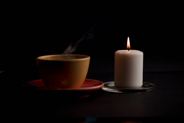 Чашку чая с горячим дымом и зажжённую свечу. на столе дома, отключение электроэнергии (сосредоточиться на чашке). - Фото, изображение