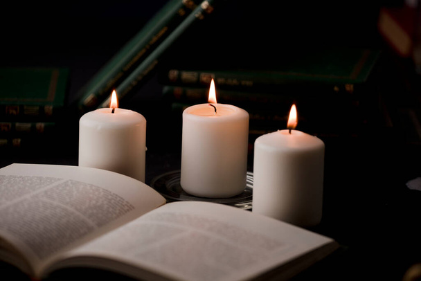 candles with flame, and reading book on desk, black background. (focus on candle). - Φωτογραφία, εικόνα