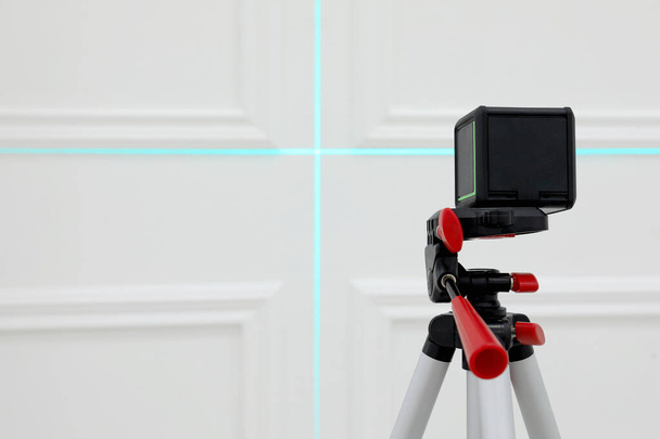 Cross line laser level on tripod in front of white wall - Foto, afbeelding