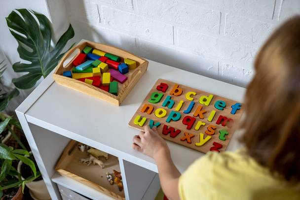 Child takes wooden letters from the shelf. English alphabet. Montessori material. Homeschooling concept. Eco friendly toy - Foto, imagen