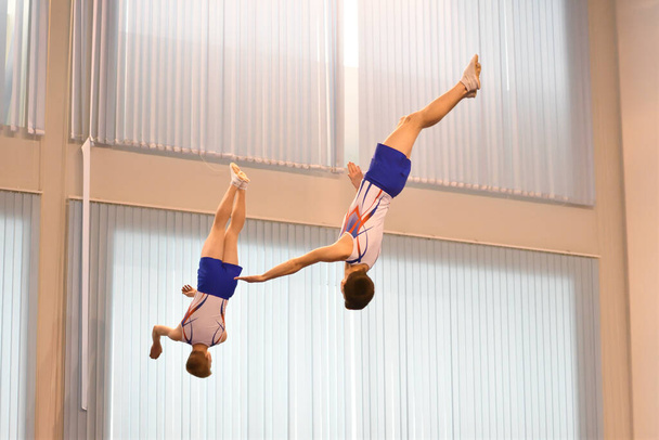 Два мальчика тренируются в синхронном прыжке на батуте  - Фото, изображение