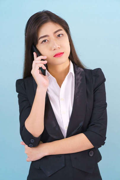 Young women in suit holding her phone standing against blue background - Foto, afbeelding