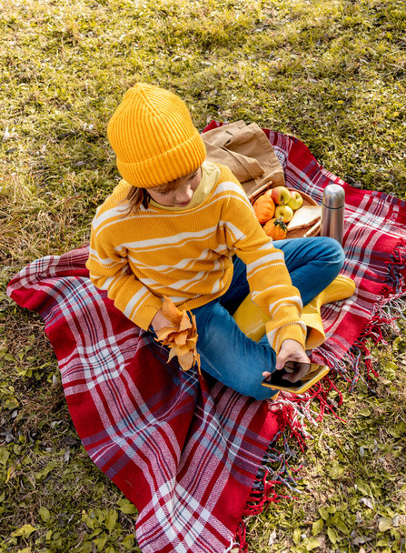 Happy girl takes video on the camera of his smartphone. Cozy slow lifestyle concept. Picnic in the meadow next to the tree. Warm up with hot drink during an autumn. - Fotoğraf, Görsel