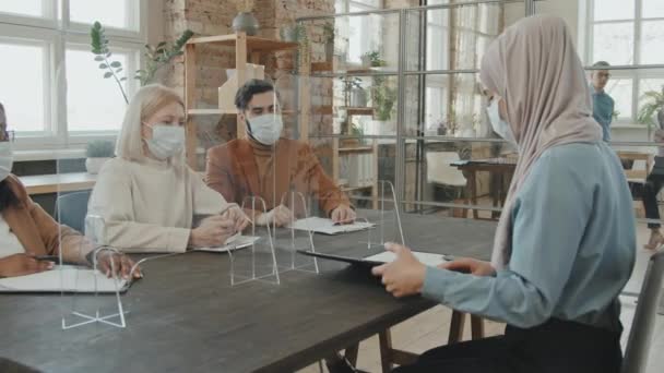 Başörtüsü ve yüz maskesi takmış Müslüman kadın iş adayının, pandemik röportajda koruyucu ekranın arkasında otururken ve şarkı söylerken çekilmiş görüntüleri. - Video, Çekim