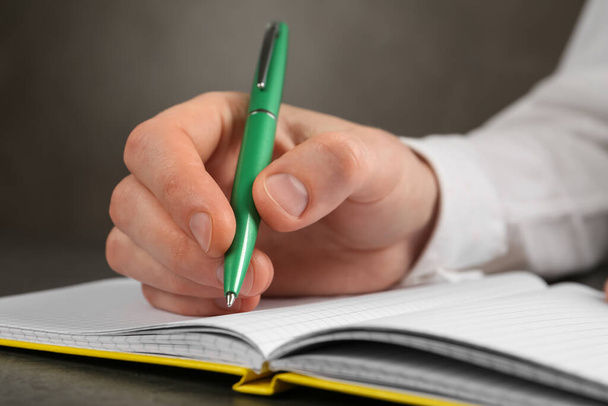 Man writing with pen in notebook at grey table, closeup of hand - Фото, зображення