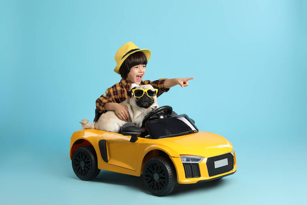 Little boy with his dog in toy car on light blue background - Photo, image