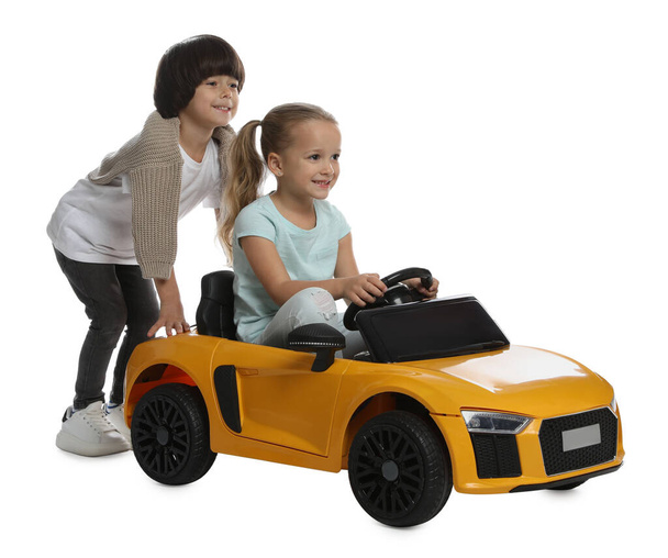 Cute boy pushing children's electric toy car with little girl on white background - Fotografie, Obrázek