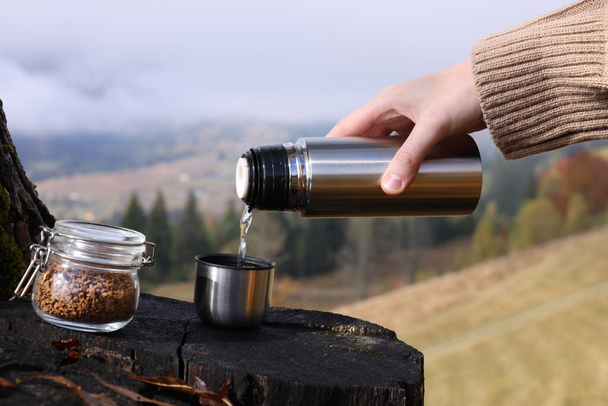 Woman pouring hot water into cup with instant coffee in mountains, closeup - Photo, Image
