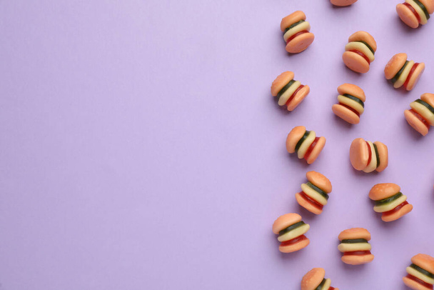 Tasty jelly candies in shape of burger on lilac background, flat lay. Space for text - 写真・画像