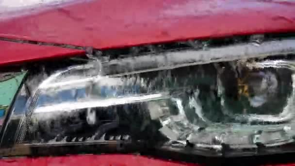 Detailní záběr vody tekoucí na reflektorech během mytí auta. Podnikový nápis - myčka aut. - Záběry, video