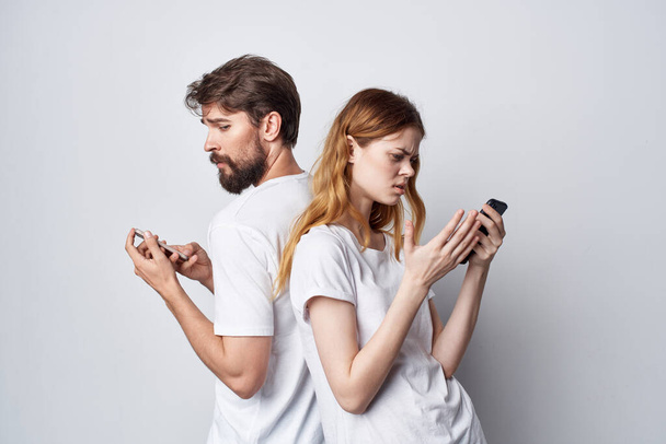 άνδρας και γυναίκα με λευκά μπλουζάκια με τηλέφωνα στα χέρια απομονωμένο φόντο - Φωτογραφία, εικόνα